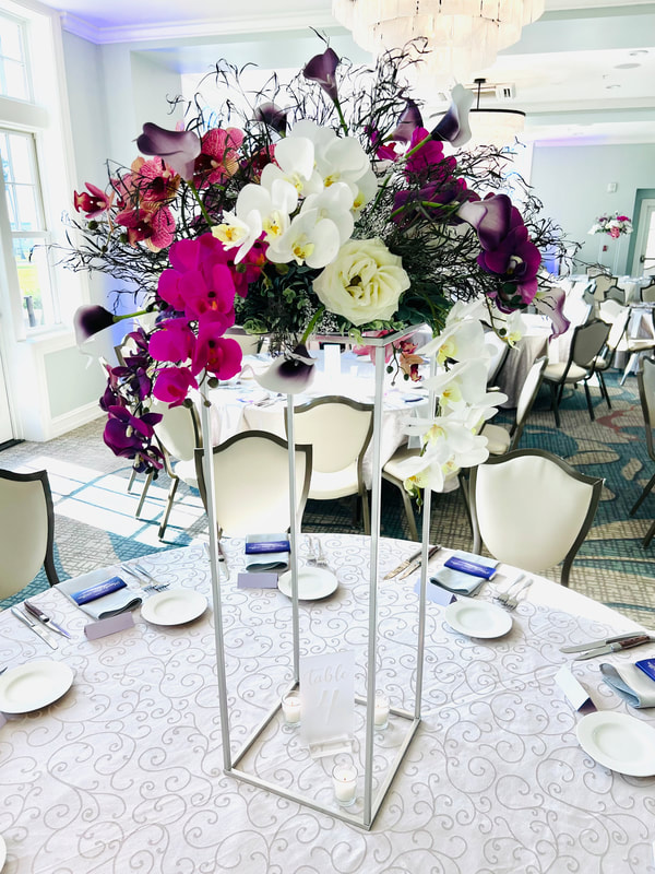 Large orchid and call lily wedding reception floral centerpiece on silver stand. Shades of purple.