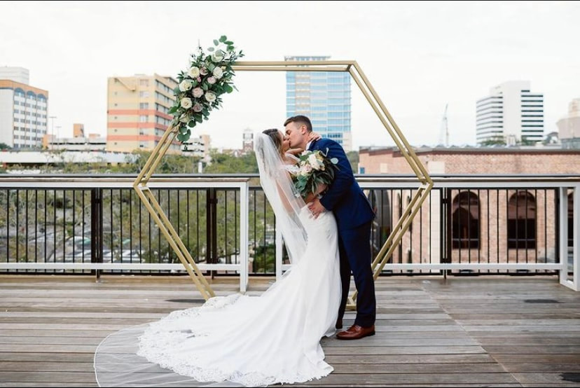 Gold geometric wedding ceremony arch with simple rustic floral design in upper corner. On rooftop of Red Mesa in St Pete, FL.