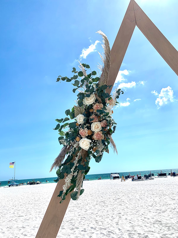 Triangle wooden arch for beach wedding ceremony with beautiful rustic flower arrange in pink and white garden blooms, accented with pampas grass.