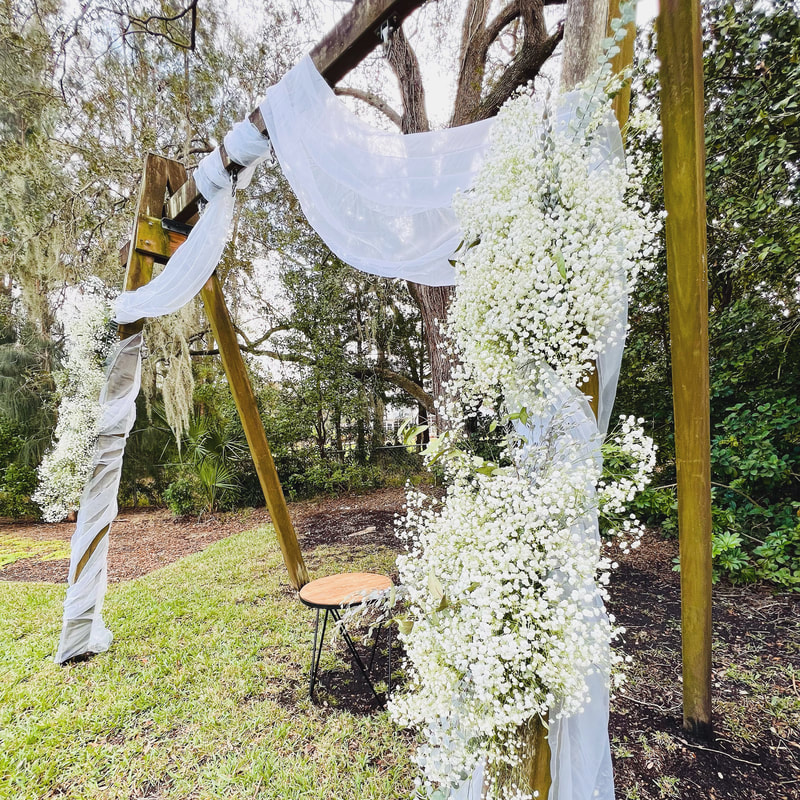 Large old swing set repurposed as ceremony arch for rustic backyard wedding. Draped with white fabric and each sided covered with baby’s breath.