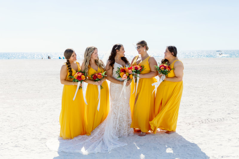 Bride and bridesmaids on beach holding vibrant tropical floral bouquets.