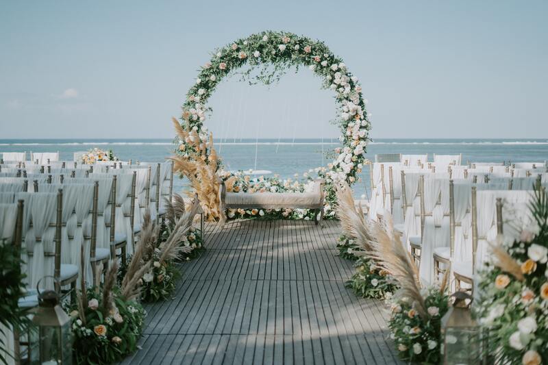 Fully covered round boho beach wedding arch flowers and aisle decor in all white. Roses and pampas grass.