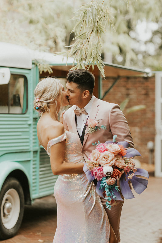 Bride and groom kiss, featuring stunning tropical pastel bridal bouquet with rustic floral accents.