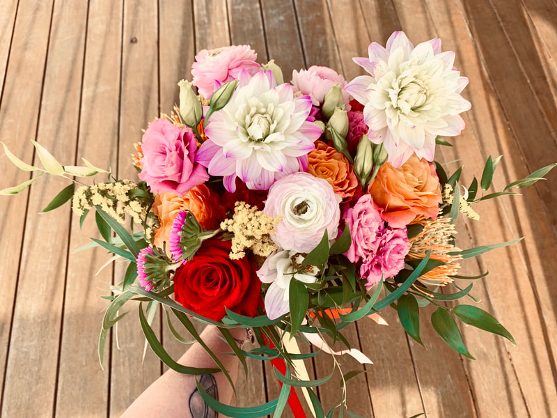 Colorful Spanish wedding bridal bouquet featuring red and orange roses, pink dahlias, yellow pin cushion proteas, and pink asters.