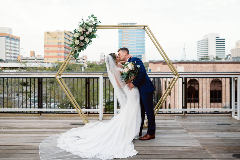 Bride and groom in front of gold wedding rustic floral arch in downtown St Pete on the rooftop of Red Mesa.