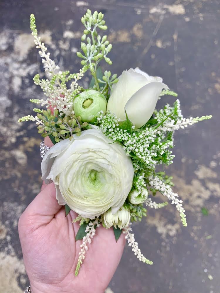 Modern white wedding wrist corsages with ranunculus, spray rose, and astilbe.